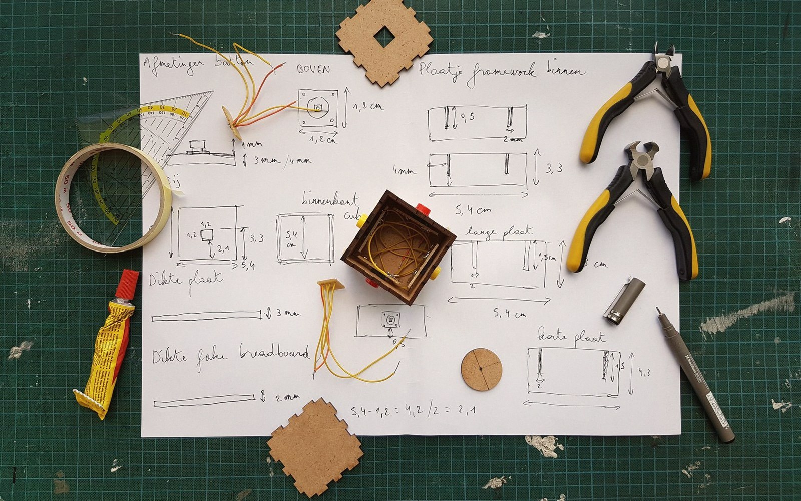 Hand-drawn wiring diagrams surround a small wooden box with coiled wire, tape and pliers nearby