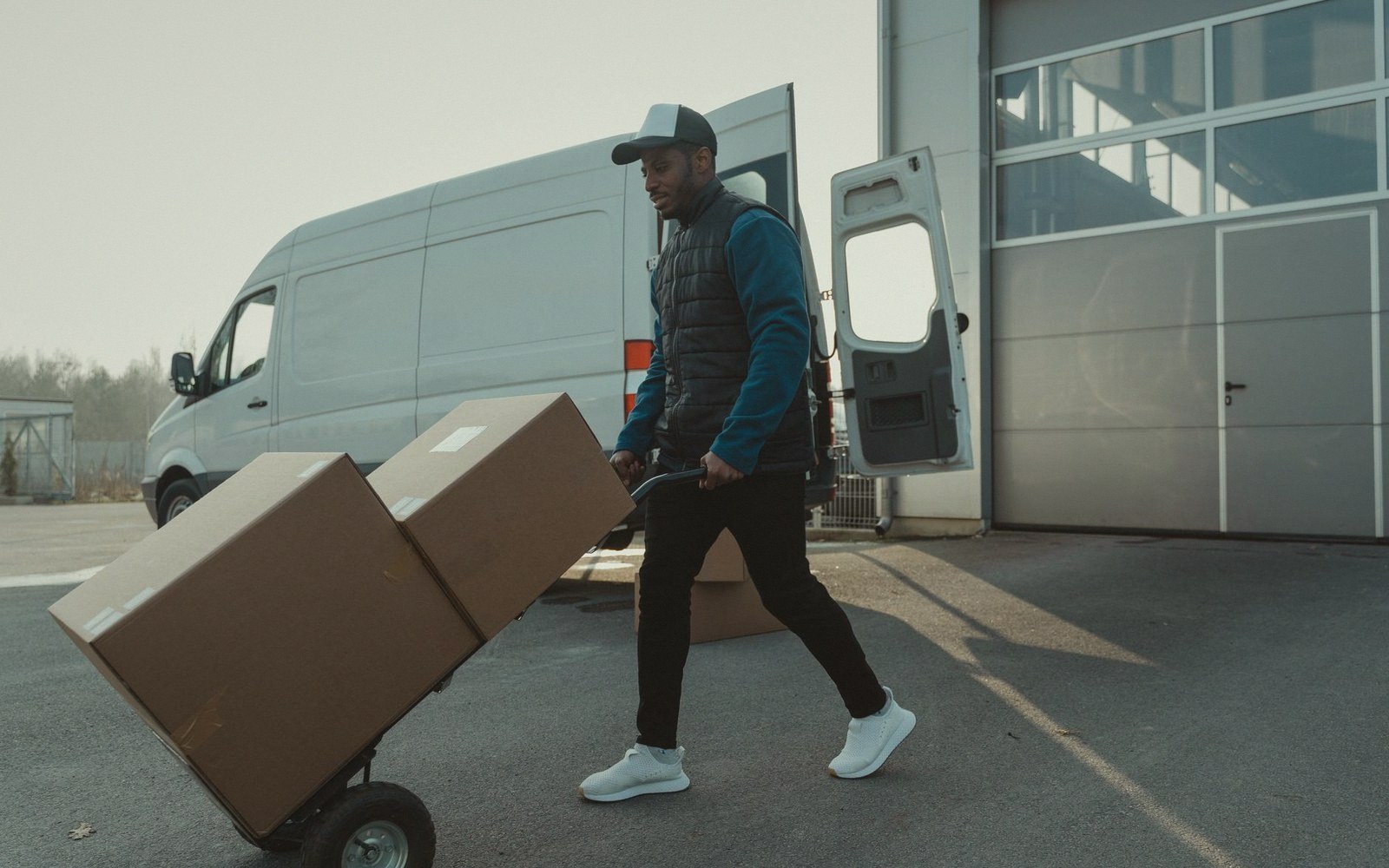 Delivery worker pushes a hand truck loaded with boxes toward a parked van