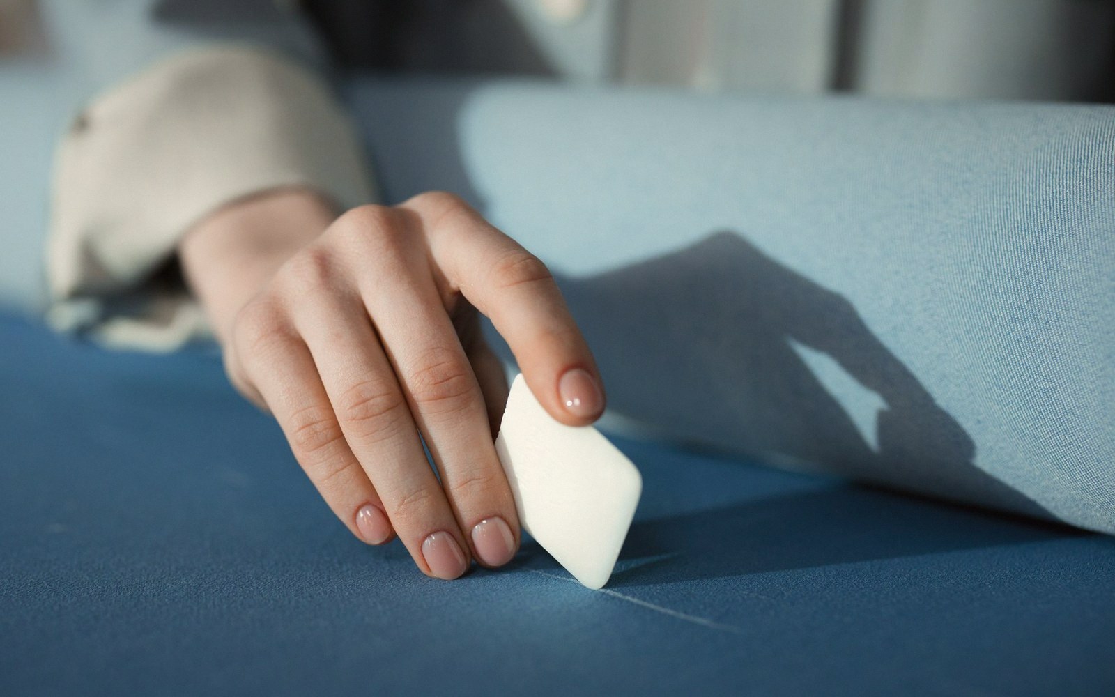 A hand holds a small eraser against a folded blue fabric surface