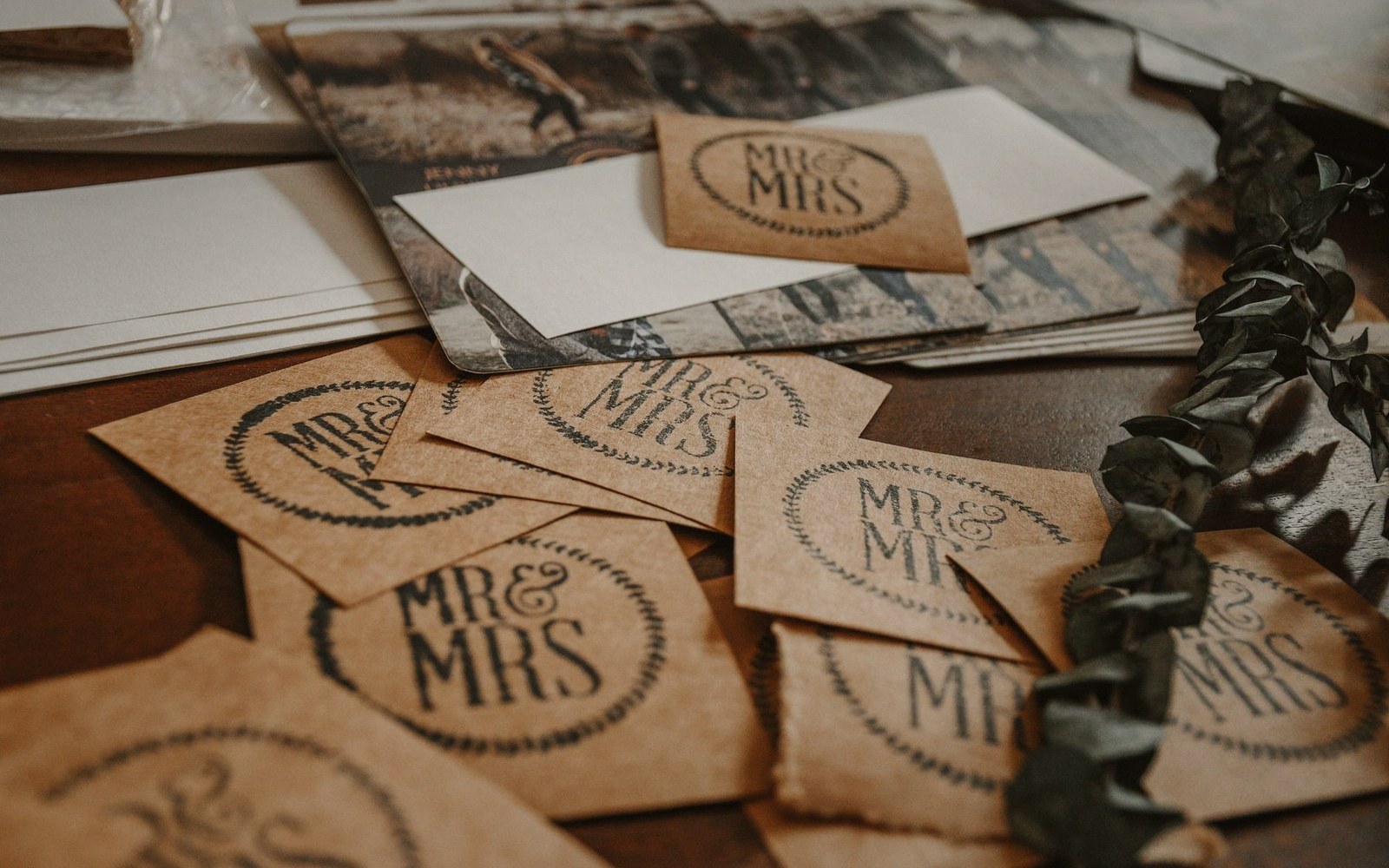 Kraft-paper "Mr & Mrs" tags scattered beside envelopes and a eucalyptus garland
